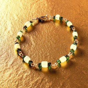 May include: A beaded bracelet featuring a gold chain with alternating light green and dark green beads. The bracelet has a lobster clasp closure. The beads are a mix of square and round shapes.