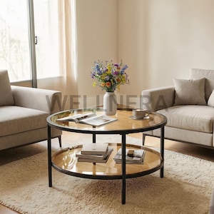 May include: A round coffee table with a black metal frame and two glass shelves. The top shelf holds a book, a cup, and a vase of flowers. The bottom shelf has books and magazines. The table is in a living room setting.
