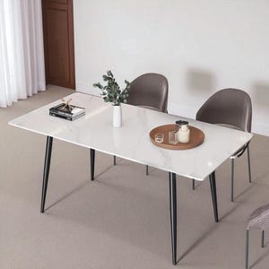 May include: A rectangular white dining table with black legs, a marble-like surface, and a small brown tray with decorative items. Two gray chairs are positioned behind the table. A vase with greenery and a book are on the table.