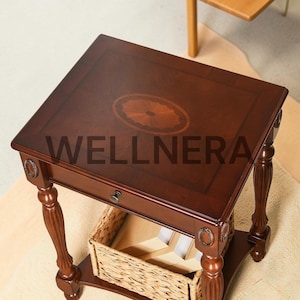 May include: A dark brown wooden side table with a rectangular top featuring a central oval inlay. The table includes a single drawer with a small knob, four fluted legs with decorative oval accents, and a lower shelf holding a woven wicker basket.