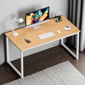 May include: A light wood-tone desk with a white metal frame. The desk has a computer monitor, keyboard, mouse, lamp, coffee cup, and smartphone on top. The desk is set on a dark wood floor with a gray rug.