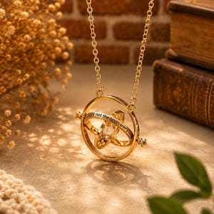May include: A gold-tone necklace with a Time Turner pendant. The pendant has a central crystal and rotating rings with engraved text. The chain is delicate, and the background includes books and decorative elements.