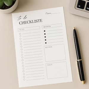 Può includere: Un elenco di cose da fare bianco con le parole "To do CHECKLISTE" in un carattere scritto a mano. L'elenco include sezioni per "To Do", "Wichtig", "Notizen" e "Fokus". Sono visibili anche una penna nera e una piccola pianta in vaso.