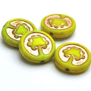 May include: Four round, lime green beads with a tree design. Each bead has a white and brown tree design in the centre. The beads are on a white background. These beads are ideal for jewellery making.