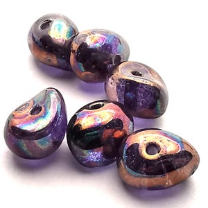 Può includere: Sei perline iridescenti a forma di goccia con un foro per infilare. Le perline hanno un colore di base viola scuro con riflessi dorati, verdi e blu scintillanti. Sono lisce e lucenti, perfette per la creazione di gioielli.