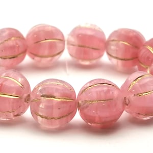 Könnte beinhalten: Eine Kette aus rosa, runden Perlen mit goldenen Streifen. Die Perlen sind durchscheinend, mit einem zarten, rosigen Farbton. Die goldenen Streifen umschließen jede Perle und verleihen einen Hauch von Eleganz. Diese Perlen sind ideal für die Schmuckherstellung.