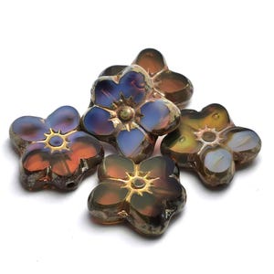 May include: Five flower-shaped beads with a metallic finish. The beads have a gradient of colors, including orange, blue, and gold. Each bead has a central gold accent. The beads are arranged on a white background.