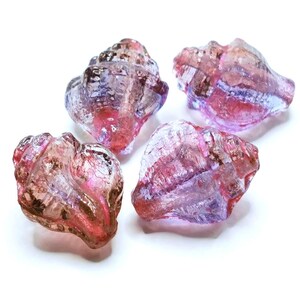 Könnte beinhalten: Vier durchscheinende, muschelförmige Glasperlen mit einem Farbverlauf in Rosa, Violett und Bernstein. Jede Perle weist eine texturierte, spiralförmige Oberfläche mit glänzendem Finish auf, die das Licht auf der facettierten Struktur reflektiert.