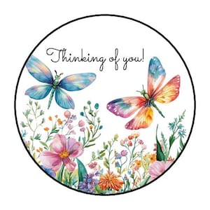 May include: Round sticker with a watercolor design featuring two dragonflies and a floral arrangement. The dragonflies have blue, pink, and orange wings. The text "Thinking of you!" is written in cursive.