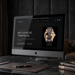 May include: A computer monitor displaying a website for Verona Mechanical Timepieces. The screen shows a gold watch with a world map dial and black leather strap. A black fountain pen rests on a leather desk mat in front of the monitor.