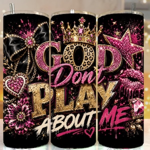 May include: A cylindrical tumbler featuring a black background with pink and gold accents. The text reads GOD DON'T PLAY ABOUT ME. Graphics include a gold crown, a large black bow, a pink heart, a flower, a star, and pink lips.