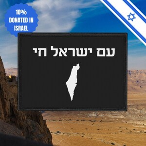 Può includere: Una toppa nera con testo ebraico bianco e un contorno bianco di Israele. La toppa ha anche un cerchio blu con la scritta "10% DONATED IN ISRAEL". Lo sfondo mostra un paesaggio desertico e un cielo blu.