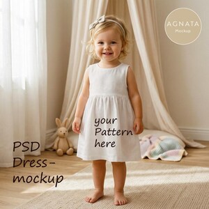 Könnte beinhalten: Ein weißes ärmelloses Kleid mit dem Text "your Pattern here" auf der Vorderseite. Das Kleid wird von einem jungen Kind getragen, das lächelt. Der Hintergrund umfasst einen beigen Teppich, ein Stoffkaninchen und ein Baldachin.