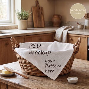 Könnte beinhalten: Ein runder geflochtener Weidenkorb mit zwei Griffen, ausgelegt mit einem weißen Stofftuch, das den schwarzen Text PSD-mockup your Pattern here trägt. Der Korb steht auf einer Holzoberfläche neben einer Butterdose und einer kleinen Schale mit Salz.