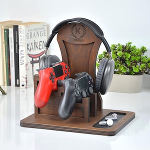 May include: A dark brown wooden gaming station featuring a black headset, two game controllers (red and black), and white earbuds. The station is engraved with the letter "K" and the name "Arora".