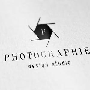 Può includere: Logo in bianco e nero per uno studio di design fotografico. Il logo presenta una forma di apertura della fotocamera stilizzata con la lettera "P" all'interno. La parola "PHOTOGRAPHIE" è stampata sotto, seguita da "design studio".