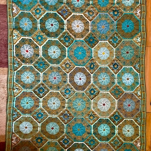Può includere: Una coperta all'uncinetto con un motivo geometrico in tonalità di verde, blu e bianco. La coperta è composta da ottagoni con disegni intricati.