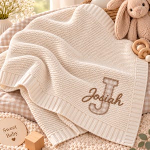 Può includere: Una coperta per neonati in maglia color crema con bordo a coste e una grande lettera J ricamata con motivo a quadretti marrone e bianco. Il nome Josiah è cucito in filo corsivo marrone sopra la lettera J sul tessuto testurizzato.