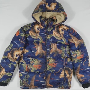 May include: A navy blue hooded puffer jacket with a vibrant print of tigers, dragons, and tropical foliage. The jacket features a full-length zipper, black cuffs, and a beige-lined hood. A stylish outerwear piece.