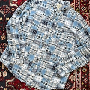 May include: A long-sleeved plaid shirt in shades of blue, white, and gray. The shirt features a button-down front, a collar, and a chest pocket. The shirt is made of a lightweight fabric.