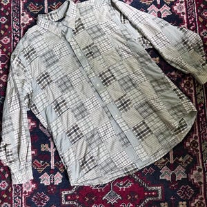 May include: A long-sleeve button-down shirt featuring a patchwork design composed of various square fabric panels in shades of beige, gray, white, and brown. The shirt includes a standard collar, a front button placket, and buttoned cuffs.