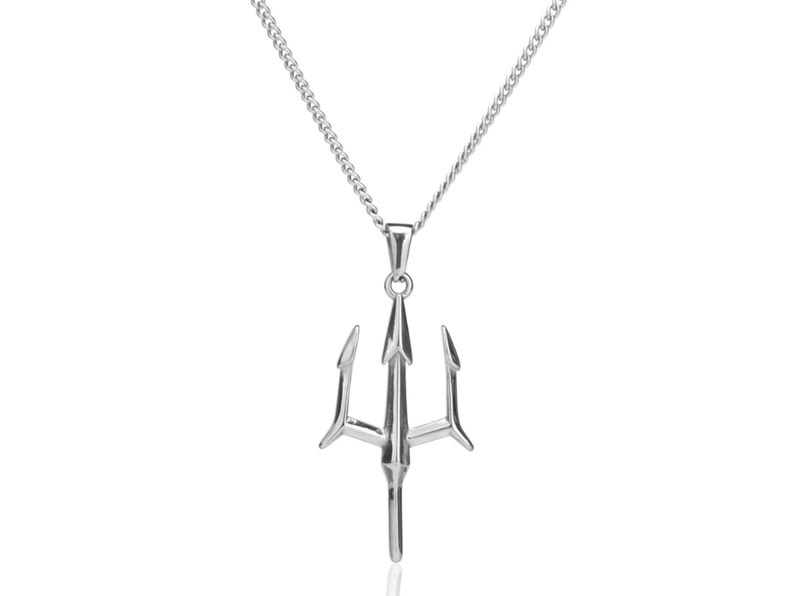 Puede incluir: Un collar con colgante plateado con un dise&ntilde;o de tridente. El tridente, una lanza de tres puntas, cuelga de una fina cadena. El collar se muestra sobre un fondo blanco liso, resaltando los detalles de la joya y el brillo del metal.