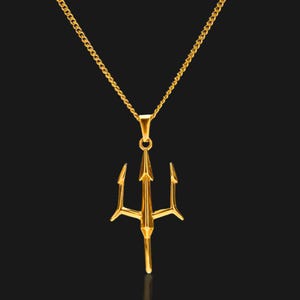 Puede incluir: Un collar con colgante dorado con dise&ntilde;o de tridente. El tridente, una lanza de tres puntas, cuelga de una delicada cadena. La joya se presenta sobre un fondo oscuro, resaltando el brillo met&aacute;lico del colgante.