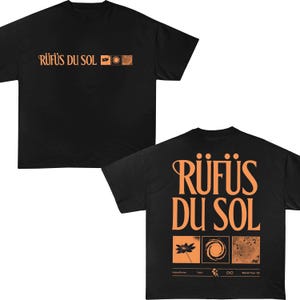 May include: A black short-sleeve t-shirt featuring the orange text RÜFÜS DU SOL on the front with three small square graphics. The back displays the same text in a larger font above three square graphics of a flower, a spiral, and texture.