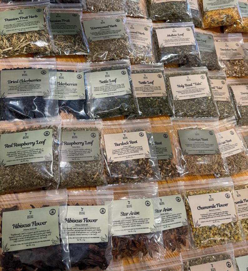 Puede incluir: Una colecci&oacute;n de bolsas de pl&aacute;stico transparente llenas de diversas hierbas, ra&iacute;ces y flores secas, cada una con una etiqueta de Seven Roots que muestra el nombre del producto y una breve descripci&oacute;n de sus usos.