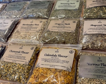 May include: A collection of clear plastic pouches filled with dried herbs and flowers, each featuring a Seven Roots label with the plant name, botanical name, and a net weight of 15g. The assortment includes Chamomile, Calendula, and Burdock.