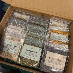 Puede incluir: Una caja de cart&oacute;n que contiene varias bolsas de pl&aacute;stico transparente llenas de hierbas y flores secas. Las etiquetas incluyen Marshmallow Root, Echinacea Herb y Lavender Flower, con un peso neto de 15g cada una.
