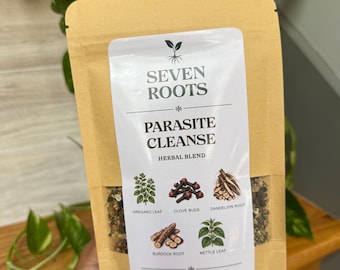 May include: A tan pouch of Seven Roots Parasite Cleanse herbal blend. The label features illustrations of oregano leaf, clove buds, dandelion root, burdock root, and nettle leaf. The text reads 1 oz | 28 g and describes a grounding herbal blend.