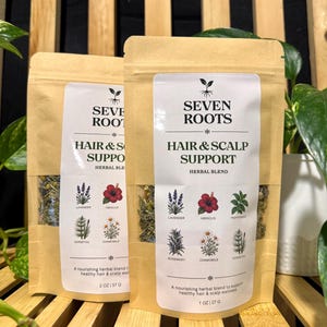 Puede incluir: Dos bolsas de papel kraft marrón claro etiquetadas como Seven Roots Hair & Scalp Support Herbal Blend. Las etiquetas muestran ilustraciones de lavanda, hibisco, menta, romero, manzanilla y cola de caballo. Una bolsa es de 57 g, la otra de 27 g.