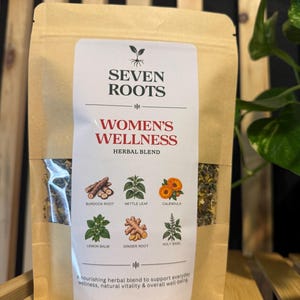 May include: A tan pouch of Seven Roots Women's Wellness herbal blend. The label features a plant icon, text, and illustrations of burdock root, nettle leaf, calendula, lemon balm, ginger root, and holy basil. The net weight is 2 oz | 57 g.