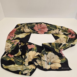 Puede incluir: Bufanda negra con un estampado floral de flores y hojas rosas, crema y verdes. La bufanda tiene la palabra "ECHO" impresa en la esquina.