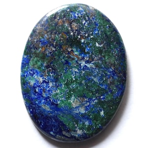 May include: Oval-shaped azurite gemstone with a polished surface. The stone features a blend of deep blue, green, and brown hues, with a marbled appearance. The gemstone is set against a white background.