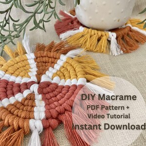 May include: Two round macrame coasters featuring a geometric pattern in white, mustard yellow, and terracotta orange. Each coaster has a fringed edge. Text on the image reads: DIY Macrame PDF Pattern + Video Tutorial Instant Download.