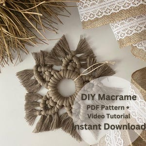 Puede incluir: Adorno de copo de nieve de macramé hecho a mano en tonos beige y marrón. El adorno tiene un centro circular con puntas radiantes y una cuerda para colgar. También se muestra cinta decorativa de arpillera con ribete de encaje blanco.