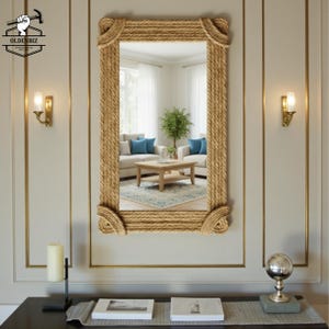 May include: A rectangular mirror with a thick rope frame, mounted on a light-colored wall. The mirror reflects a living room with a sofa, coffee table, and blue cushions. Decorative sconces flank the mirror.