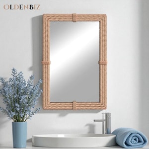 May include: Rectangular mirror with a rope-style frame. The frame is a light tan color, and the mirror is mounted on a white wall. The mirror is above a white sink, with a blue towel and a blue vase with flowers.
