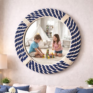 Puede incluir: Un espejo redondo con un marco de cuerda azul marino y crema. El espejo refleja una habitación con niños jugando. El espejo está montado en una pared de color claro. Tema náutico.