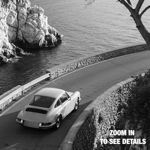 A vintage white sports car is driving on a winding coastal road, with a rocky cliff and the ocean in the background.