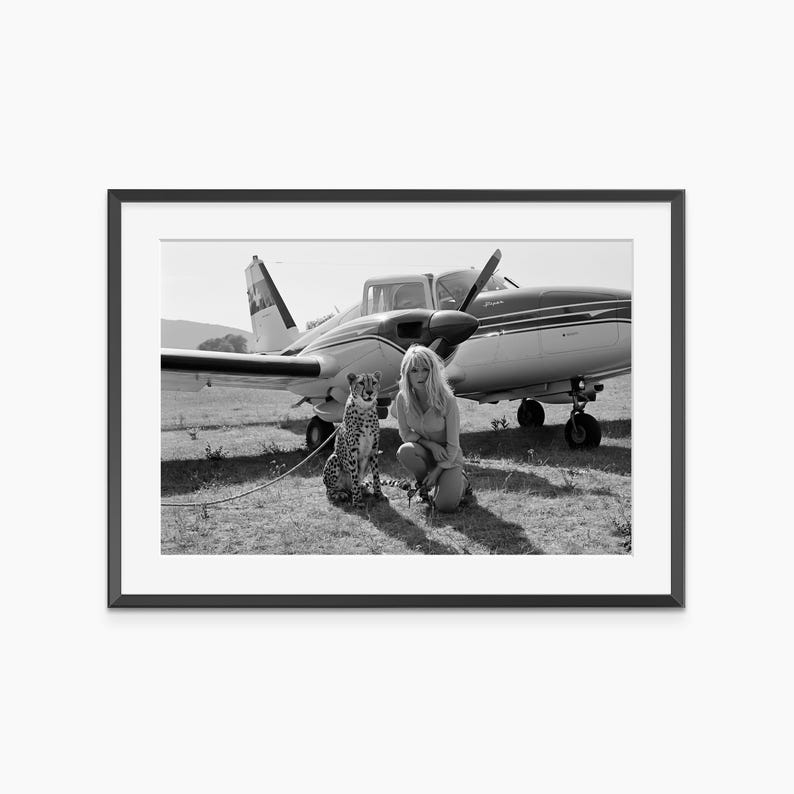 A black and white photograph of a woman kneeling next to a cheetah in front of an airplane.