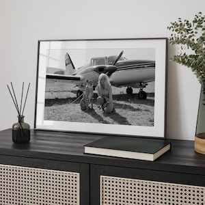 A framed black and white photograph of a woman and a cat, with a small airplane in the background, is displayed on a wooden cabinet.