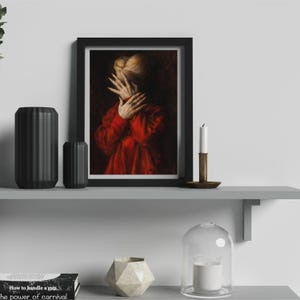 May include: Framed artwork featuring a person in a red garment, hands covering the face. The painting has a dark, moody aesthetic. The artwork is displayed on a gray shelf with black vases, a candle, and a decorative object.