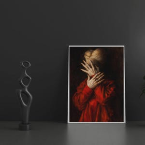 May include: A framed art print featuring a person in a red garment, hands covering the face. The artwork has a dark, dramatic aesthetic. A black abstract sculpture stands to the left of the print.