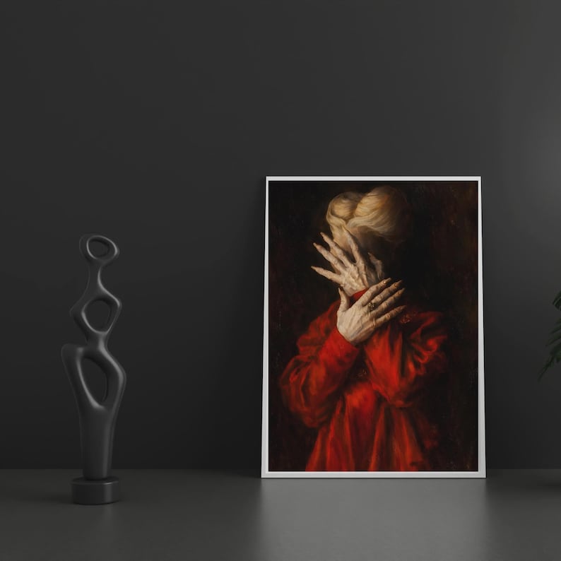 May include: A framed art print featuring a person in a red garment, hands covering the face. The artwork has a dark, dramatic aesthetic. A black abstract sculpture stands to the left of the print.