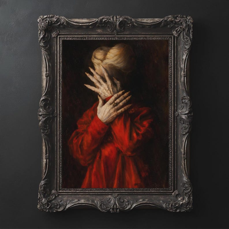 May include: A framed portrait depicts a person in a red garment, hands covering the face. The person's blonde hair is visible. The ornate, dark gray frame adds a vintage aesthetic to the artwork.