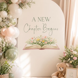 May include: A decorative backdrop with the text "A New Chapter Begins" above an open book illustration with flowers. The scene includes a teddy bear, balloons, and floral arrangements, creating a soft, welcoming atmosphere for a baby shower or similar event.