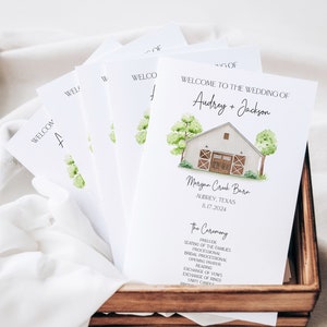 May include: Wedding ceremony programme with a watercolour illustration of a white barn with brown doors and green trees. The programme includes the names Audrey and Jackson, the date 8.17.2024, and the location Morgan Creek Barn, Aubrey, Texas.
